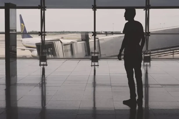 Person standing near airport windows with luggage at a terminal in the United States