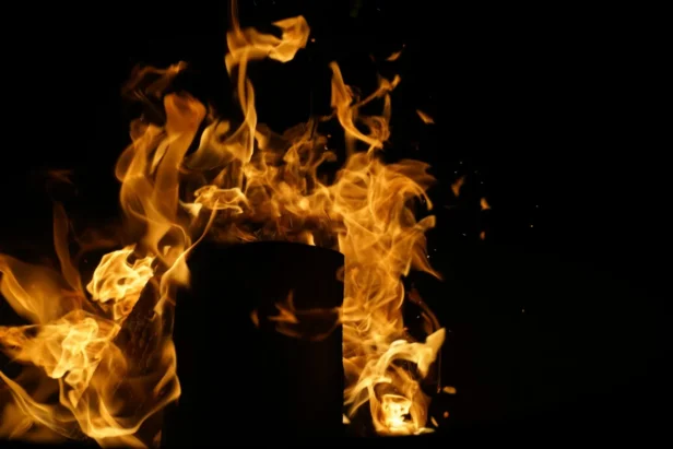 Flames engulfing wooden structure exterior, fiery explosion from incendiary device attack.