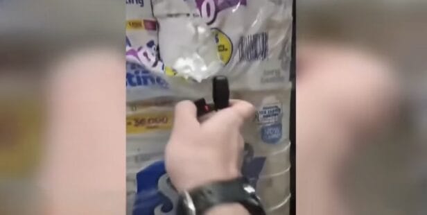 A worker films himself setting fire to a massive toilet paper warehouse filled with stacked rolls and industrial equipment.